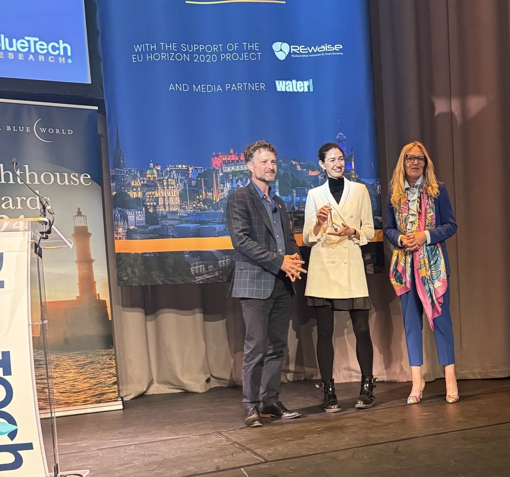 Photograph showing BlueTech CEO Paul O'Callaghan on stage handing the Lighthouse Award to Microsoft Water Program Manager Paulina Concha Larrauri and FIDO CEO Victoria Edwards.